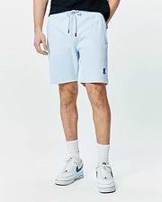 Mens Keith Short 8 light blue pique knit shorts, relaxed fit, featuring a drawstring waist with black tips, side pockets, and a small embroidered navy Psycho Bunny skull logo on the left leg.