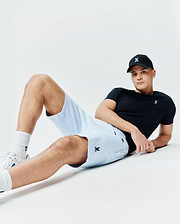Black classic fit jersey t-shirt with small white embroidered Psycho Bunny skull logo on chest, light blue pique Mens Keith Short with navy embroidered logo on thigh, and black baseball cap with white logo.
