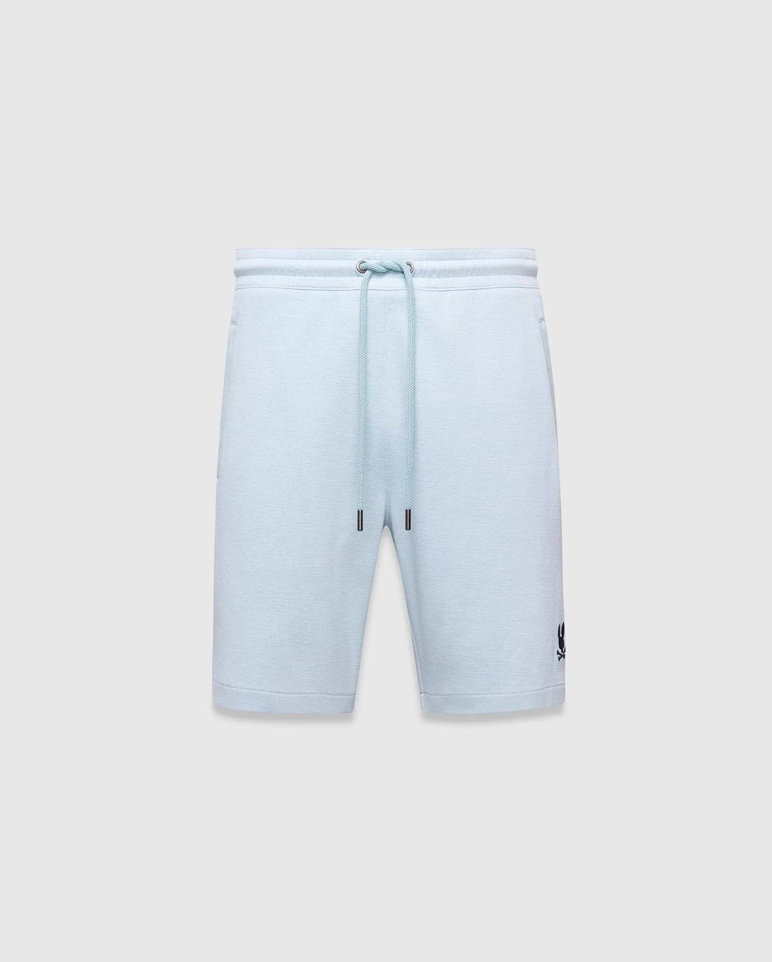 Mens Keith Short 8 light blue pique knit shorts, relaxed fit, featuring a drawstring waist with silver eyelets and dark blue tips, and a small embroidered dark blue Psycho Bunny skull logo on the lower left leg.
