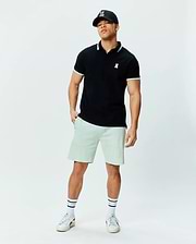 Black pique polo with white tipped collar and cuffs, featuring a small white embroidered Psycho Bunny skull logo on the chest. Paired with relaxed fit light green Mens Keith Short 8 in soft knit.