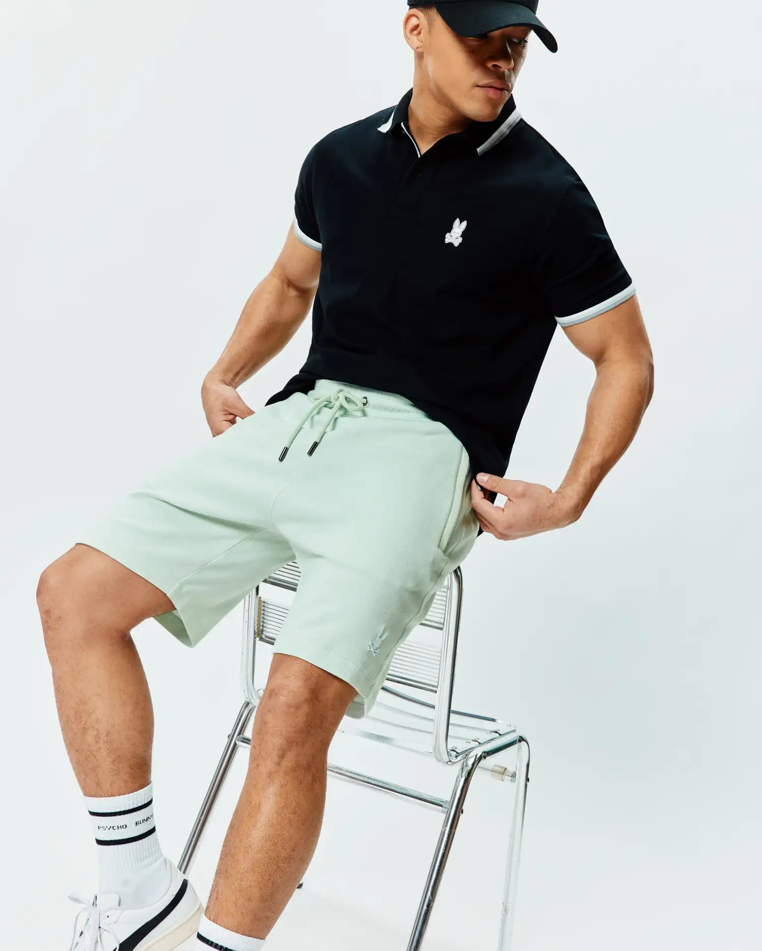 Black classic pique polo with white collar, grey/white striped cuffs, and embroidered Psycho Bunny chest logo. Paired with Mens Keith Short 8, light green textured shorts featuring a drawstring waist and leg logo.