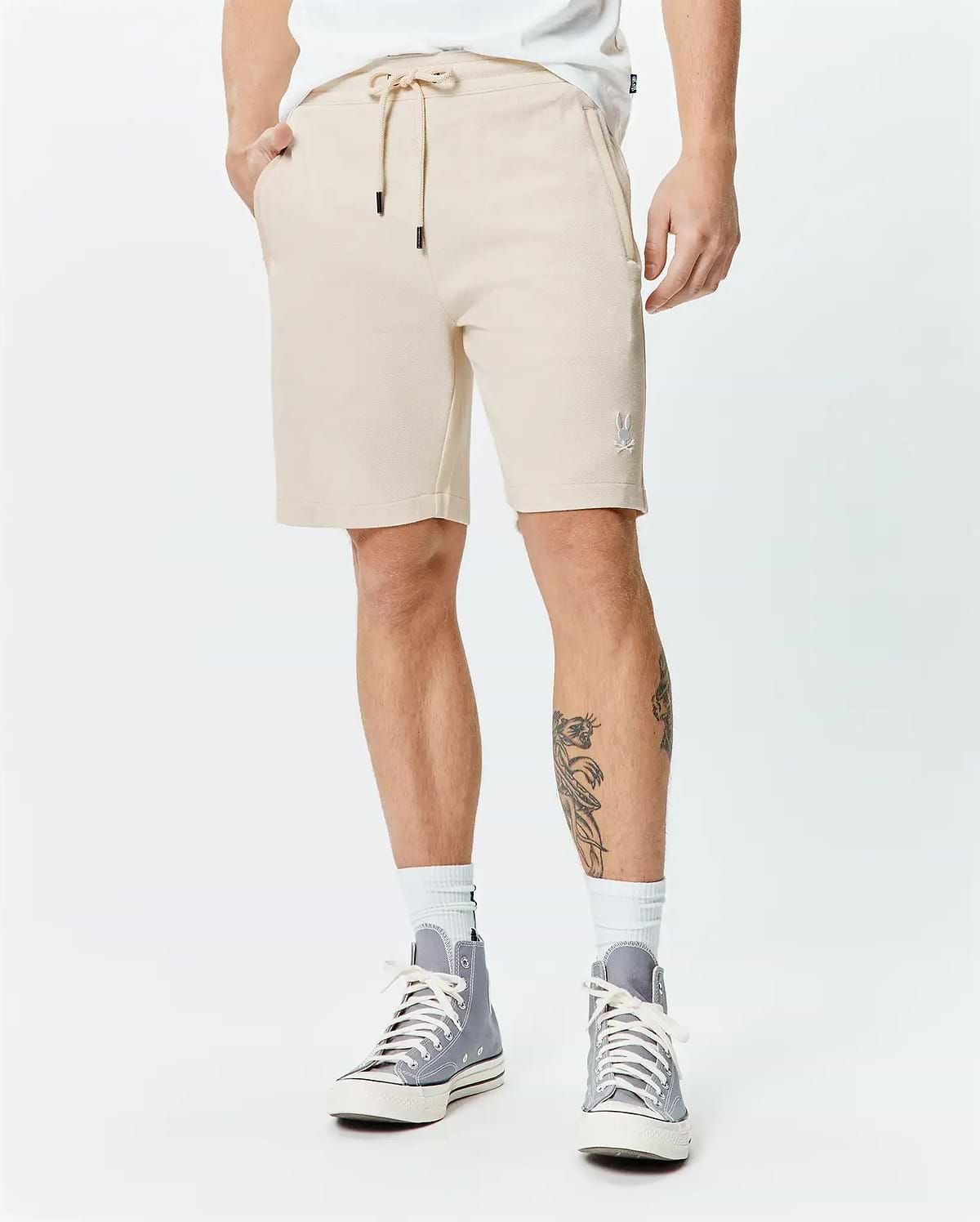 Mens Keith Short 8, sand pique knit, relaxed fit shorts with drawstring waist, black tips, and a small white embroidered Psycho Bunny skull logo on the left thigh.