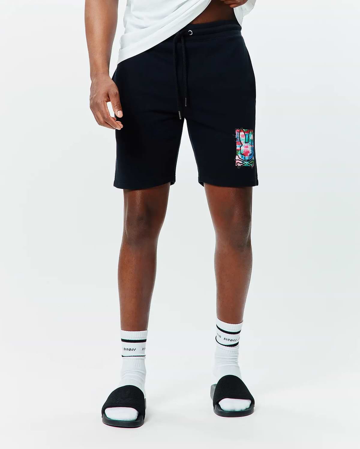Mens Isaac Print Short, black relaxed fit French terry shorts with a drawstring waist, featuring a large, vibrant multi-color Psycho Bunny skull graphic print on the left thigh.