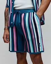 Mens Cliff Knit Short with vibrant teal, pink, light blue, white, and navy vertical stripes. Features a ribbed knit texture, drawstring waist, and small embroidered Psycho Bunny skull logo on the lower right leg. (2)