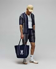 Mens Cliff Knit Short and matching knit polo, both navy with cream vertical stripes, a tan cap, white socks, and a navy tote bag, all featuring the iconic embroidered Psycho Bunny skull logo. (3)