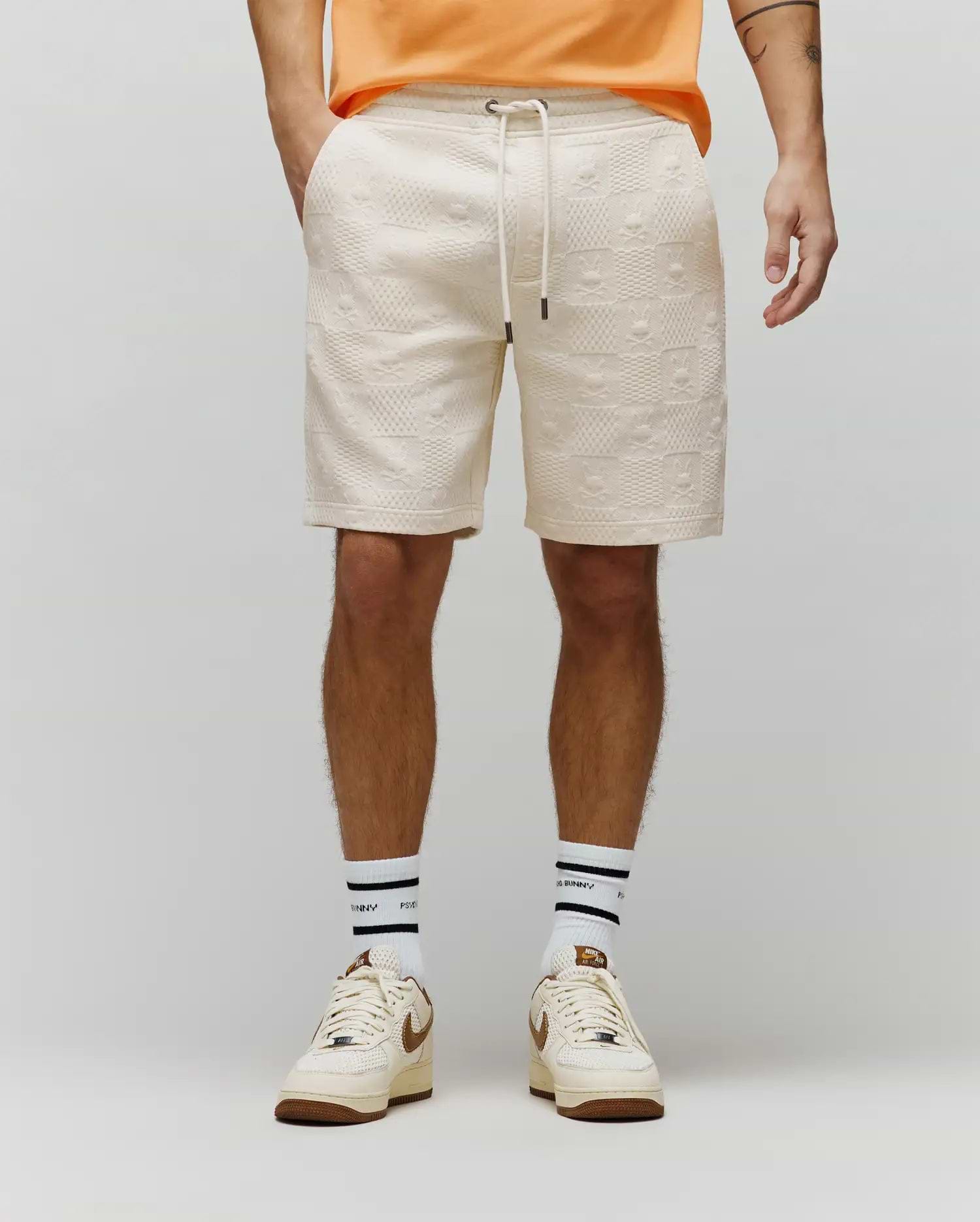 Cream relaxed fit textured knit Mens Dustin Sweatshort with an all-over embossed Psycho Bunny skull logo and checkered pattern, featuring a drawstring waist.