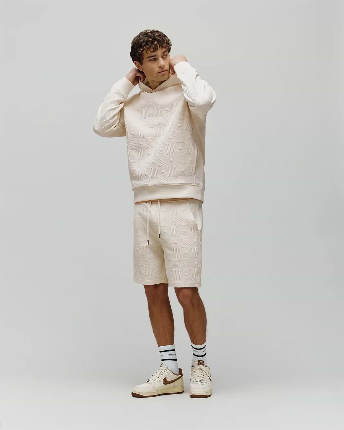 Mens Dustin Sweatshort and matching relaxed fit cream hoodie, both with an allover embossed Psycho Bunny skull logo pattern. Small embroidered bunny logo on hoodie chest, black drawstring tips.