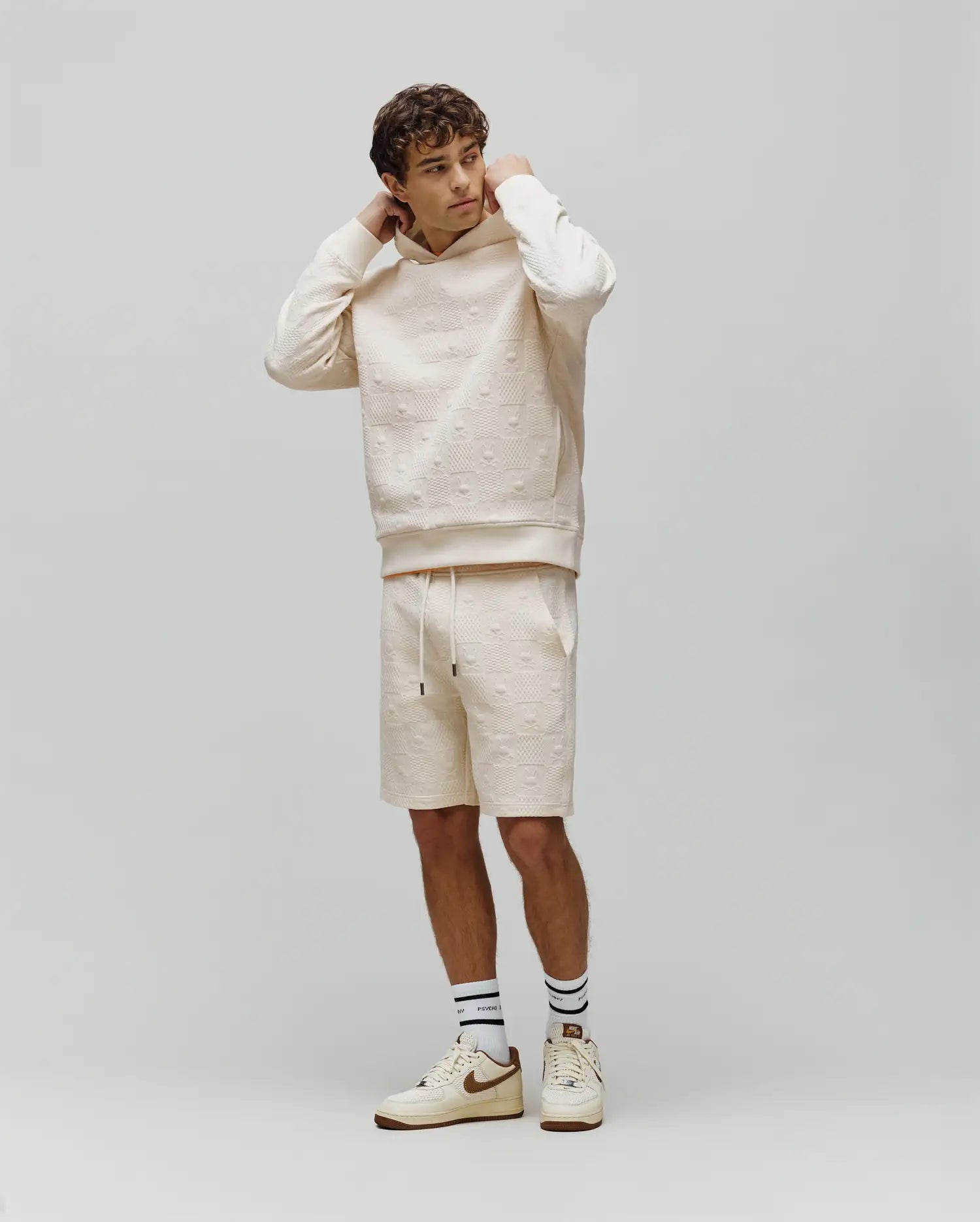 Mens Dustin Sweatshort and matching relaxed fit cream hoodie, both with an allover embossed Psycho Bunny skull logo pattern. Small embroidered bunny logo on hoodie chest, black drawstring tips.