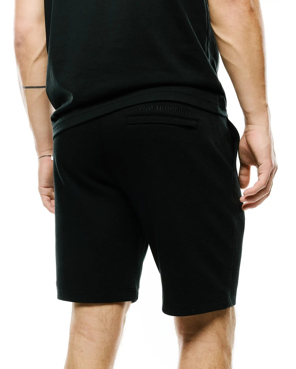 Mens Marc Textured Short, a black, relaxed-fit short crafted from a distinctive textured knit fabric, featuring subtle tonal embroidered Psycho Bunny branding on the back waistband.