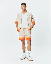 Beige knit short-sleeve shirt and matching Mens Holden Knit Short 6, both featuring a wavy knit texture with vibrant orange accents and a small embroidered orange Psycho Bunny skull logo on the shirt's chest.
