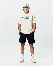 Cream classic fit jersey t-shirt with bold green PSYCHO BUNNY chest text, paired with black Mens Devon Knit Short, a cream and green Psycho Bunny skull logo cap, and white logo socks.