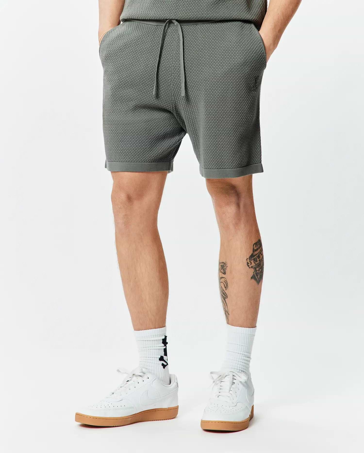 Mens Devon Knit Short 7 in dark olive green, featuring a textured knit fabric, drawstring waist, and a small embroidered Psycho Bunny skull logo on the left thigh, with a relaxed fit.
