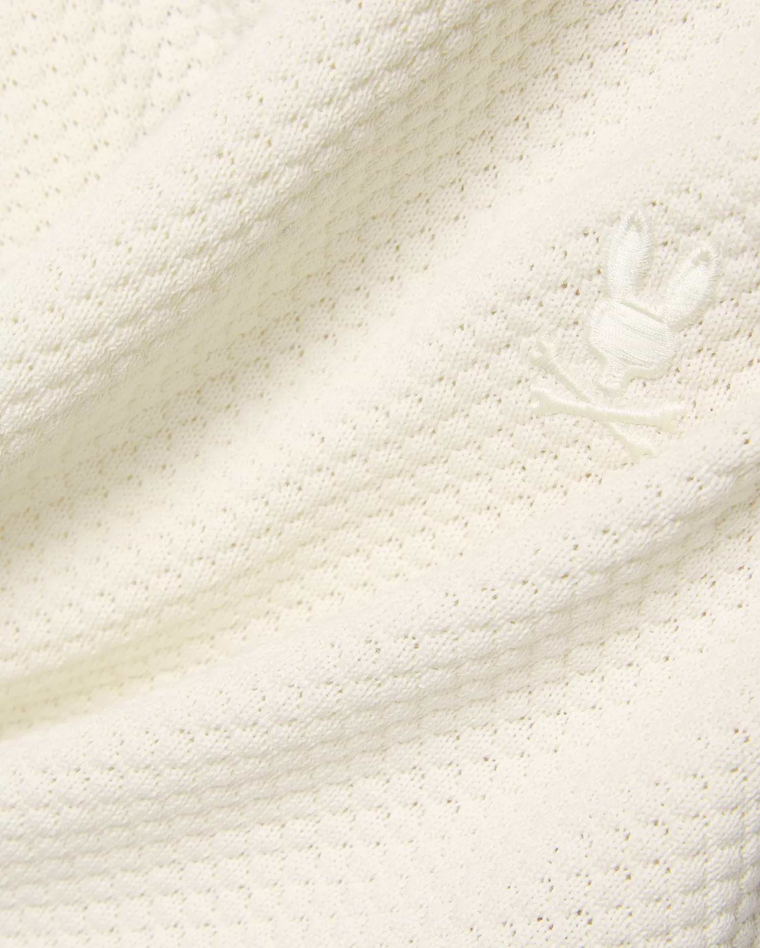 Mens Devon Knit Short in premium cream, featuring a soft, subtly patterned open knit fabric and a small, tone-on-tone embroidered Psycho Bunny skull logo detail.
