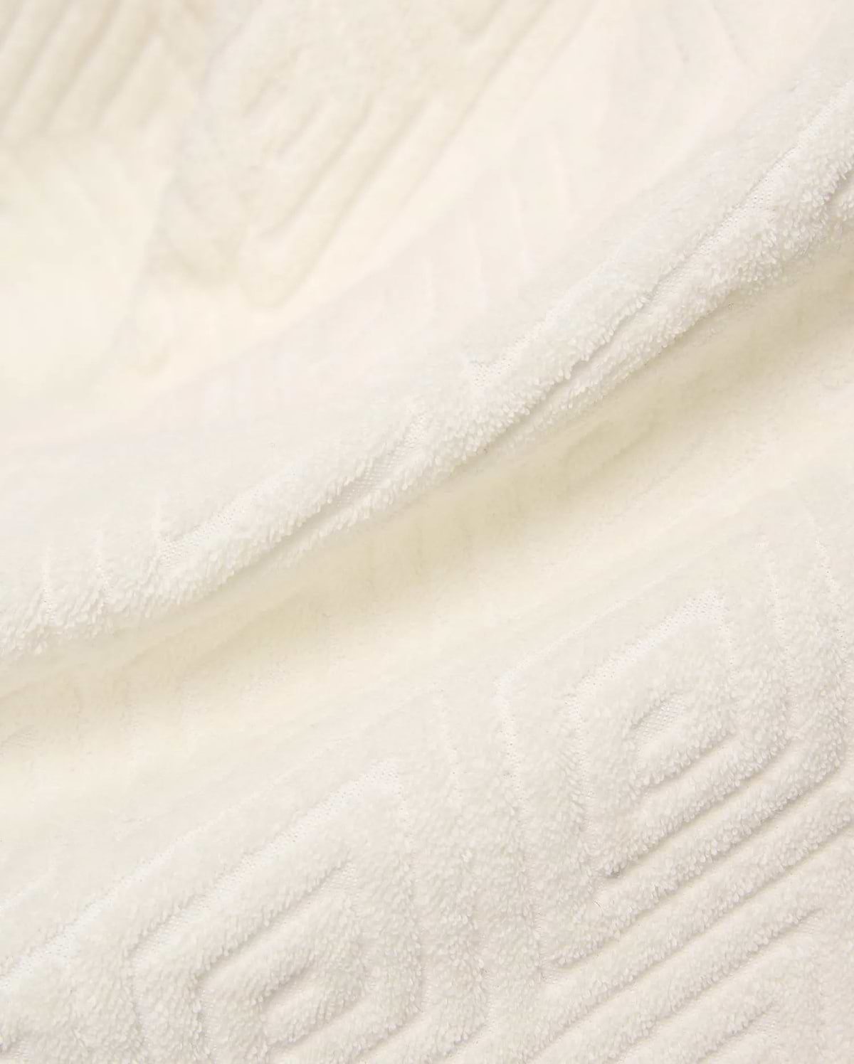 Creamy white Mens Tristan Short crafted from plush, absorbent terry cloth, featuring an intricate, subtly embossed geometric square and spiral pattern throughout the luxurious fabric.