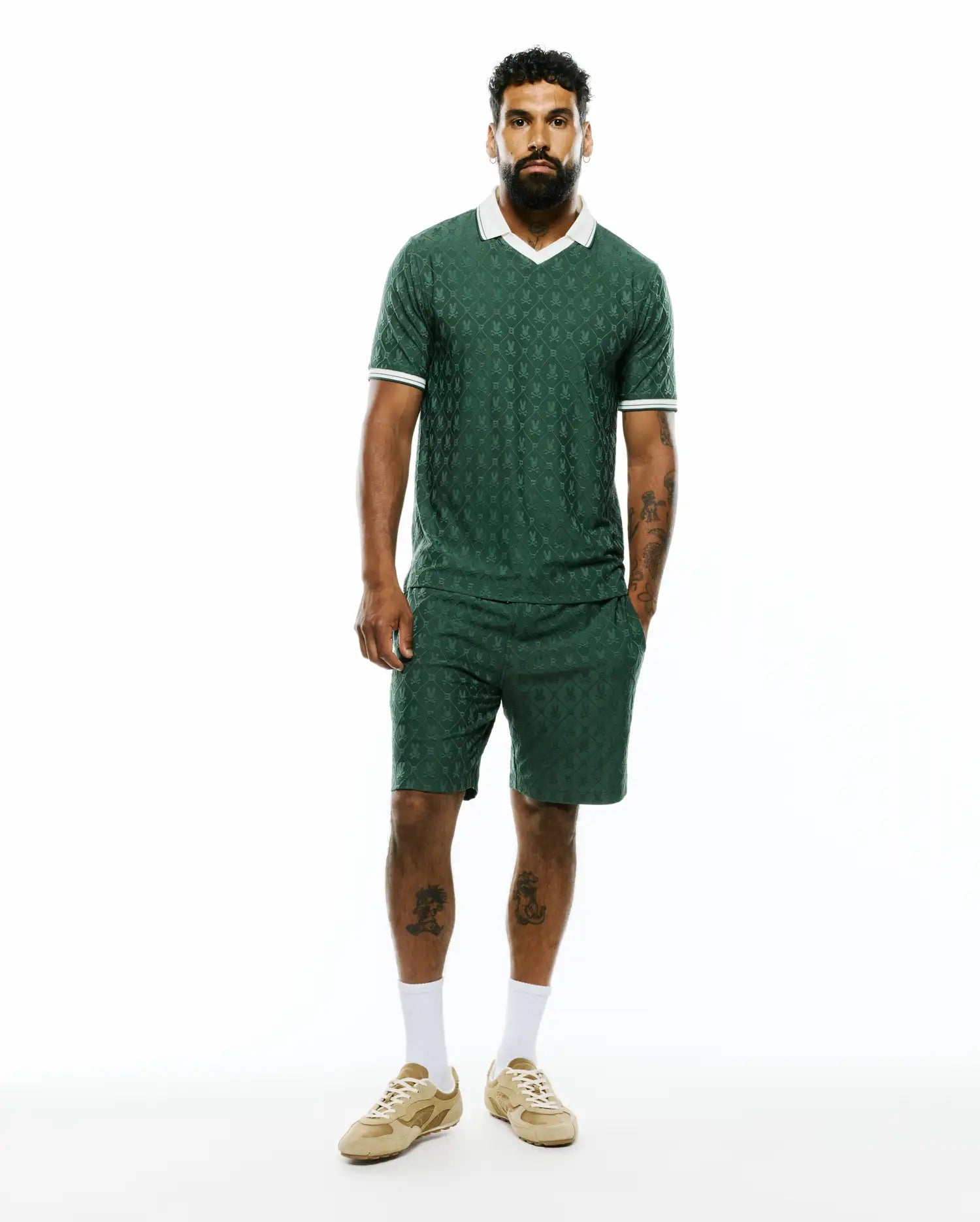 Dark green jacquard knit polo and matching Mens Garry Jacquard Sweatshort, both featuring an all-over Psycho Bunny skull pattern, white V-neck collar, and striped cuffs.