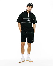 Black short-sleeve quarter-zip top with white chest stripes and embroidered Psycho Bunny logo, paired with MENS STEVIE SHORT featuring white side piping and vertical logo. Includes logo cap and socks.
