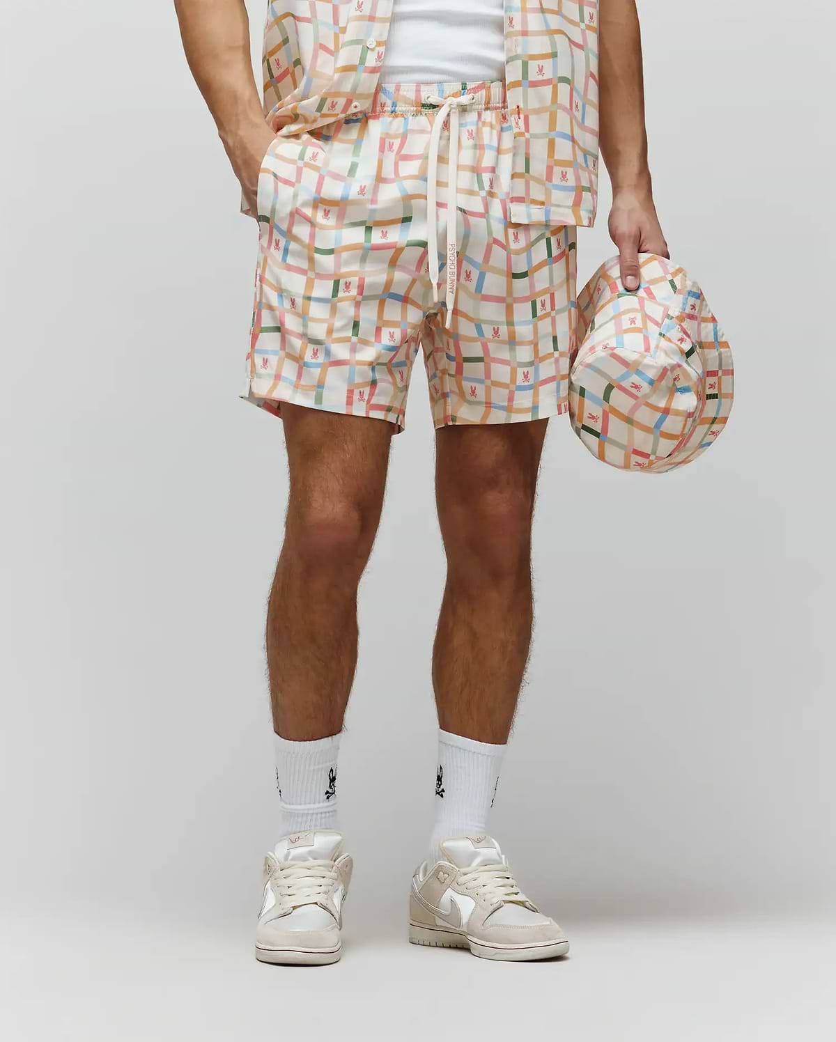 Mens Atlas Swim Trunk in cream with a vibrant multicolor plaid pattern, featuring small repeated Psycho Bunny skull logos and PSYCHO BUNNY text on the drawstring. Relaxed fit, smooth quick-dry fabric.