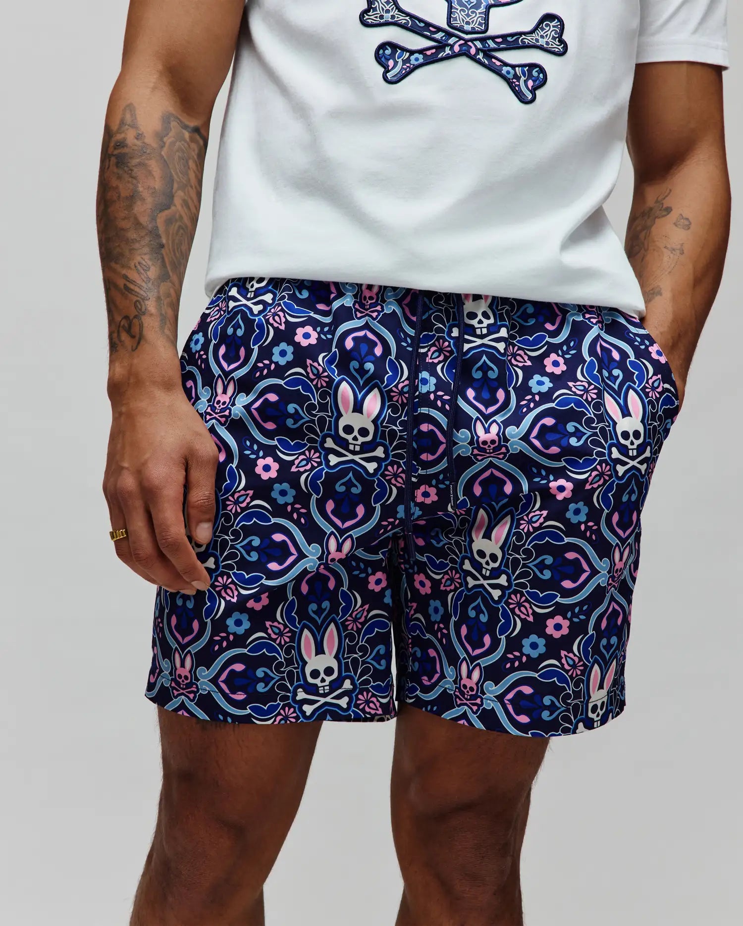 Mens Luke Swim Trunk in navy with an allover intricate floral and paisley pattern featuring repeated pink, light blue, and white Psycho Bunny skull logos, classic fit, smooth quick-dry fabric.