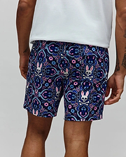 Mens Luke Swim Trunk in navy blue with an all-over ornate floral and paisley pattern featuring repeated Psycho Bunny skull logos with pink ears, crafted from smooth, quick-dry fabric in a classic fit.