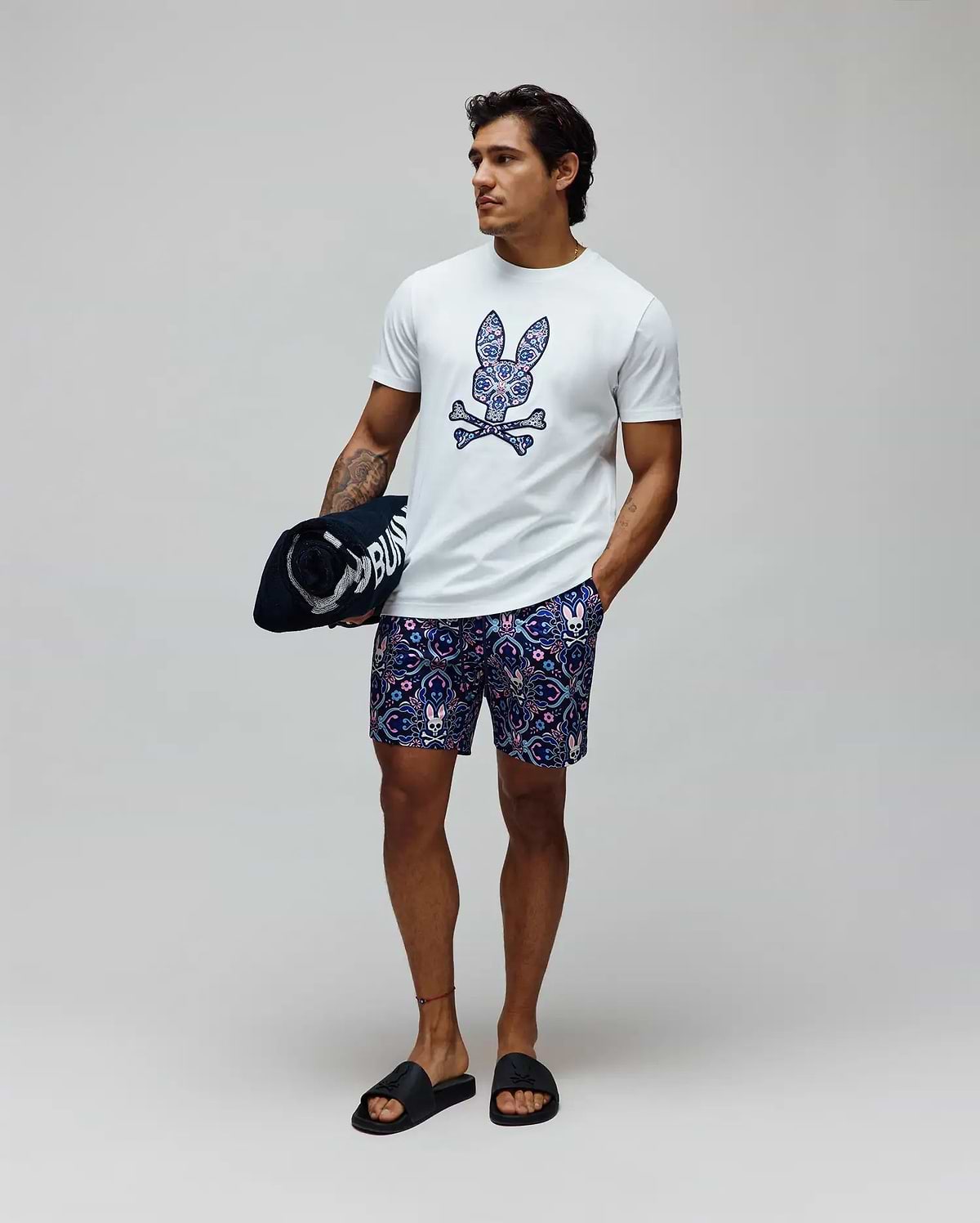 White classic fit jersey t-shirt with a large, colorful paisley Psycho Bunny skull logo on the chest, and Mens Luke Swim Trunk in navy with an all-over intricate pattern featuring small bunny skulls.