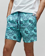 Mens Luke Swim Trunk in aqua, with a navy blue bandana paisley print featuring Psycho Bunny skull logos, a relaxed fit, smooth quick-dry fabric, and a small Psycho Bunny tag on the right hip.