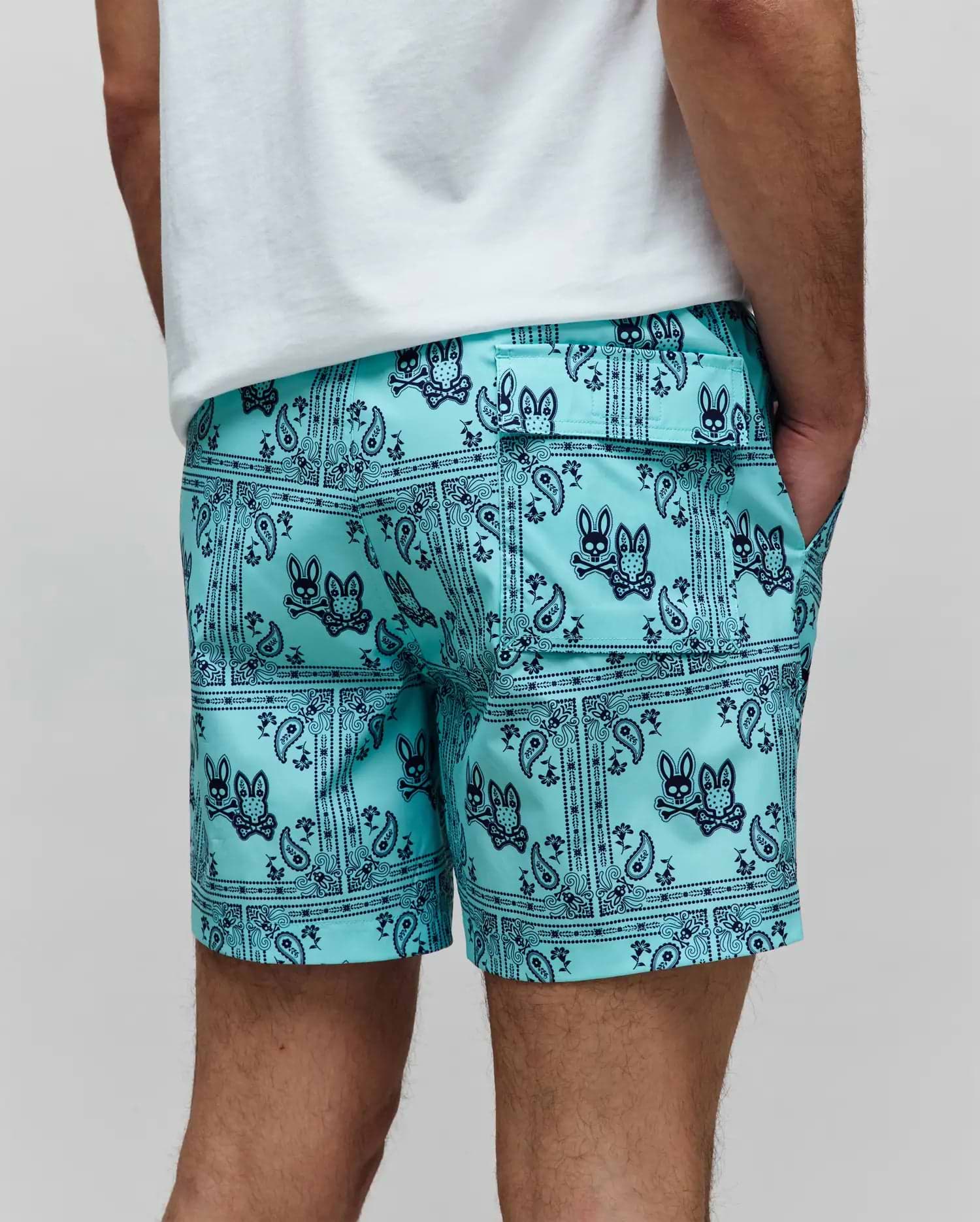 Mens Luke Swim Trunk in aqua with a navy blue all-over bandana paisley print featuring the iconic Psycho Bunny skull logo, relaxed fit, smooth quick-dry fabric, with side and back flap pockets.