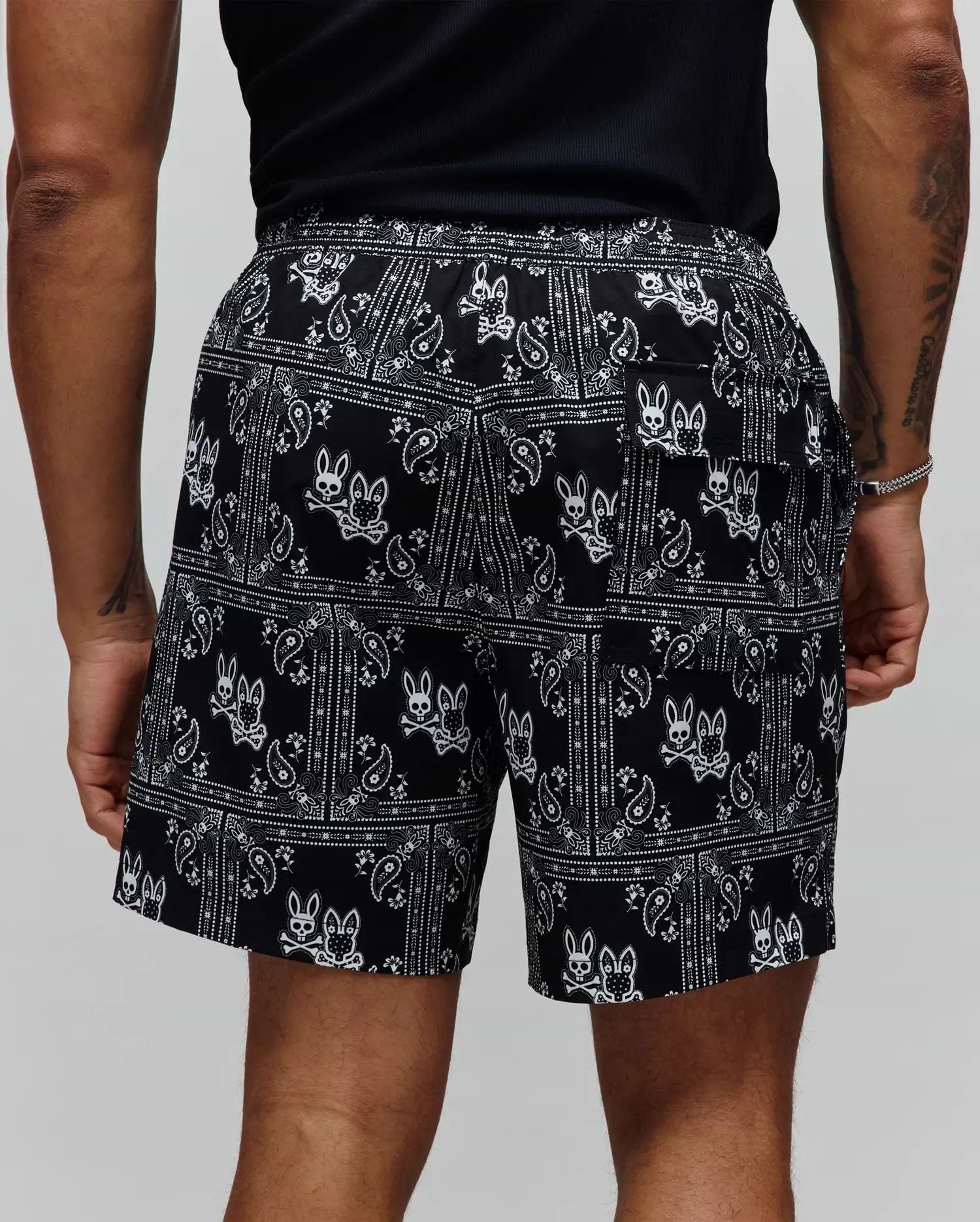 Mens Luke Swim Trunk in black with a white all-over bandana paisley print and repeated Psycho Bunny skull logos, featuring a relaxed fit and smooth fabric.