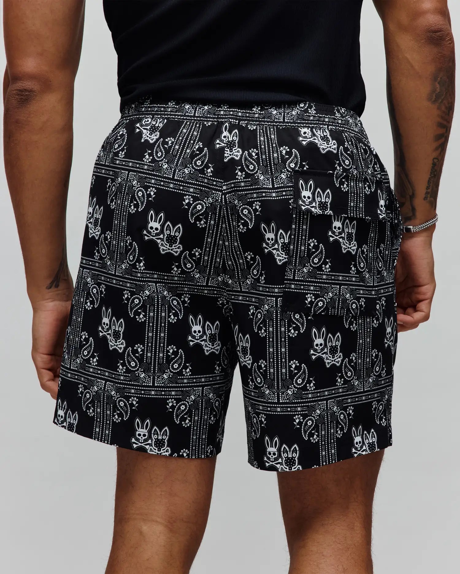Mens Luke Swim Trunk in black with a white all-over bandana paisley print and repeated Psycho Bunny skull logos, featuring a relaxed fit and smooth fabric.