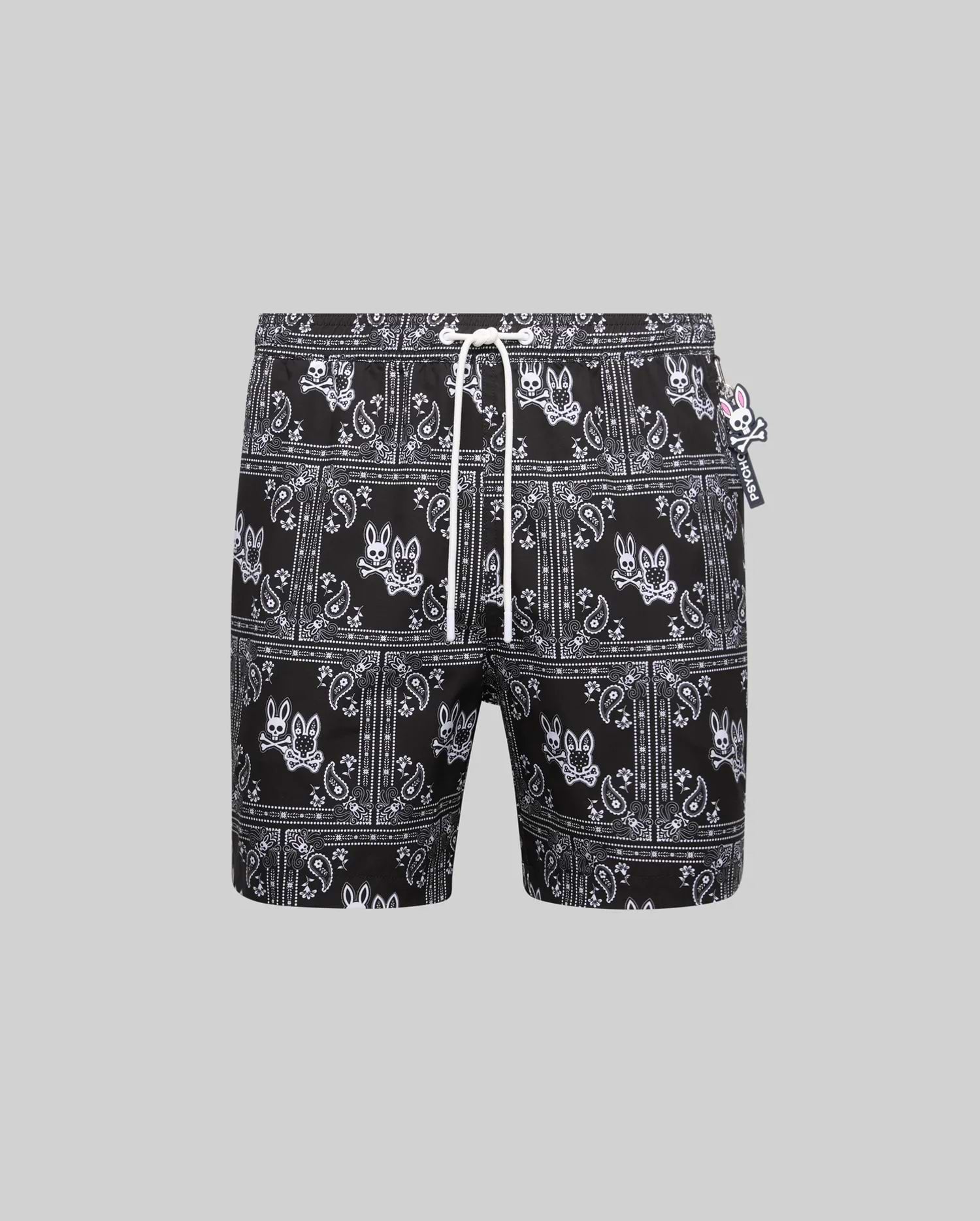 Mens Luke Swim Trunk, black with white all-over bandana print featuring the iconic Psycho Bunny skull logo, relaxed fit, smooth quick-dry fabric, white drawstring, and small Psycho Bunny tag.