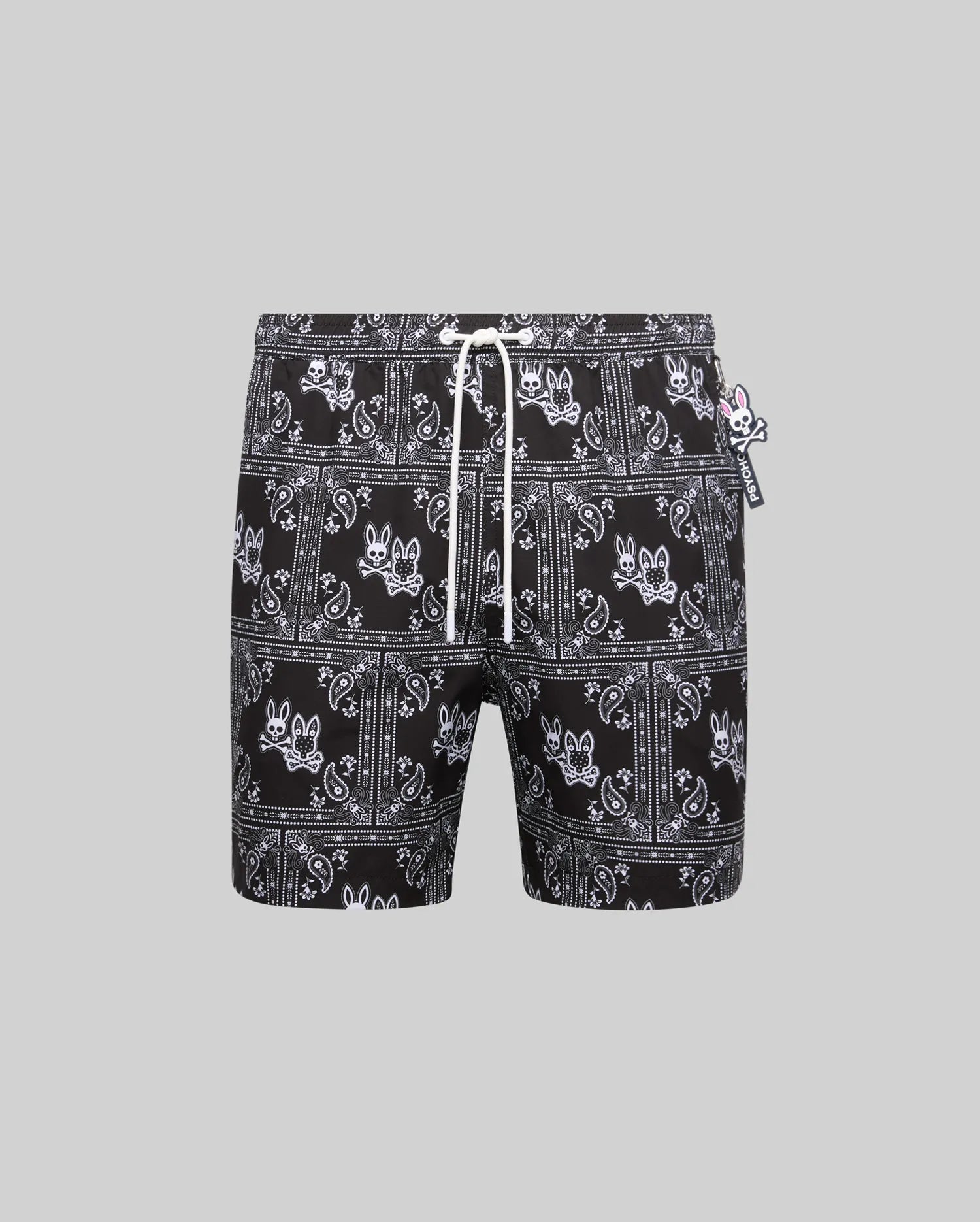 Mens Luke Swim Trunk, black with white all-over bandana print featuring the iconic Psycho Bunny skull logo, relaxed fit, smooth quick-dry fabric, white drawstring, and small Psycho Bunny tag.
