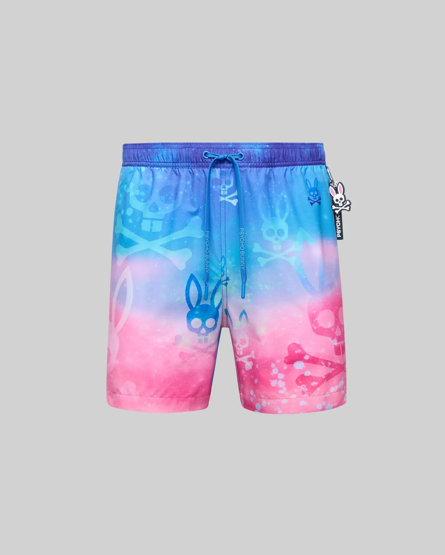Mens Caspian Swim Trunk, relaxed fit, quick-dry fabric, vibrant blue to pink gradient with all-over bunny skull and skull & crossbones pattern, plus a small Psycho Bunny logo on the drawstring.