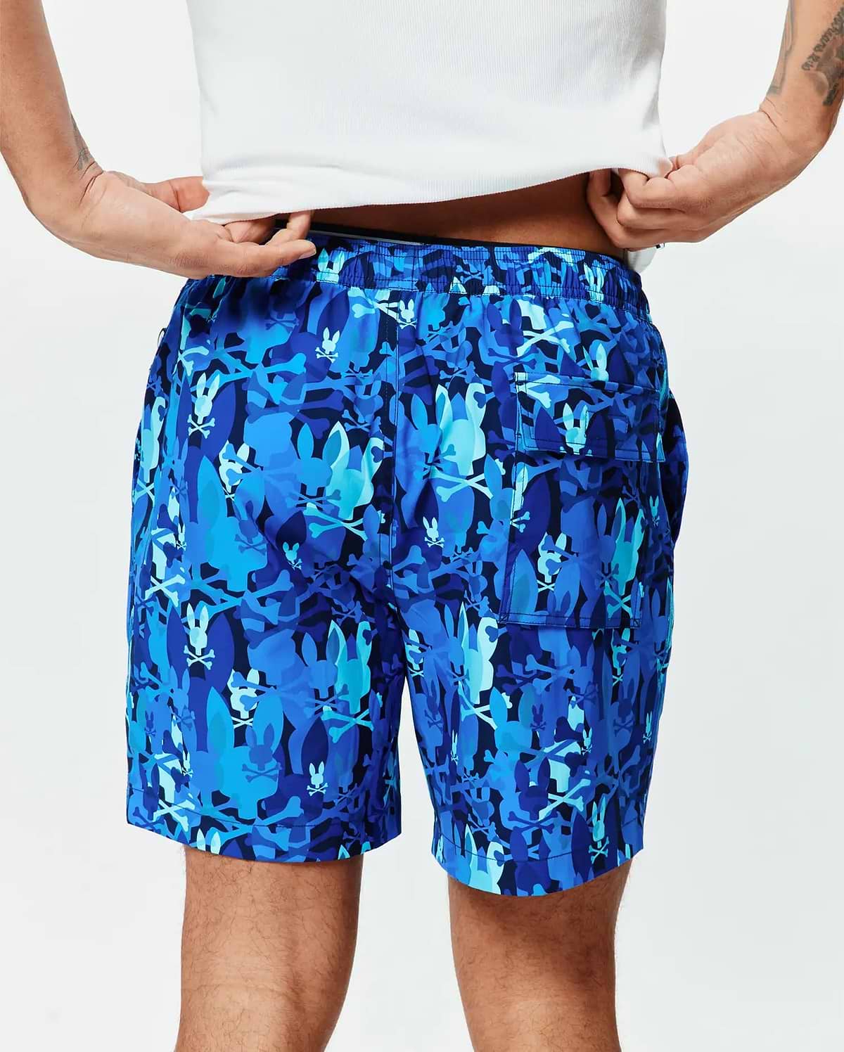 Mens Tanner Swim Trunk in a vibrant blue camouflage pattern, with repeated Psycho Bunny skull logos, an elastic waistband, back flap pocket, and a relaxed fit in smooth, quick-dry fabric.