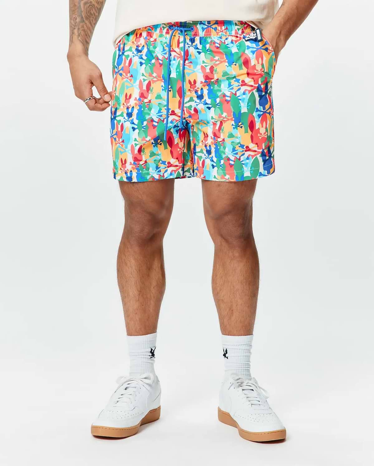 Mens Tanner Swim Trunk featuring a vibrant all-over print of colorful Psycho Bunny skull logos, crossbones, and abstract shapes, with a blue drawstring and a classic fit.