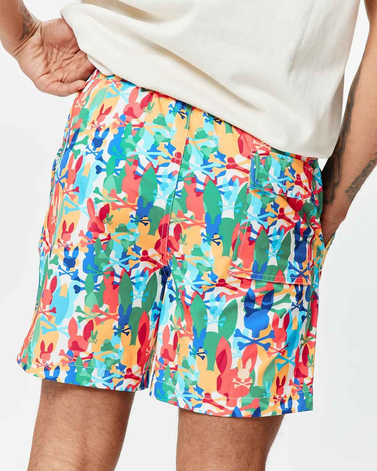 Mens Tanner Swim Trunk in a vibrant multi-color all-over print featuring Psycho Bunny skull logos, surfboards, and crossbones on a white background, crafted from smooth, quick-dry fabric with a relaxed fit.