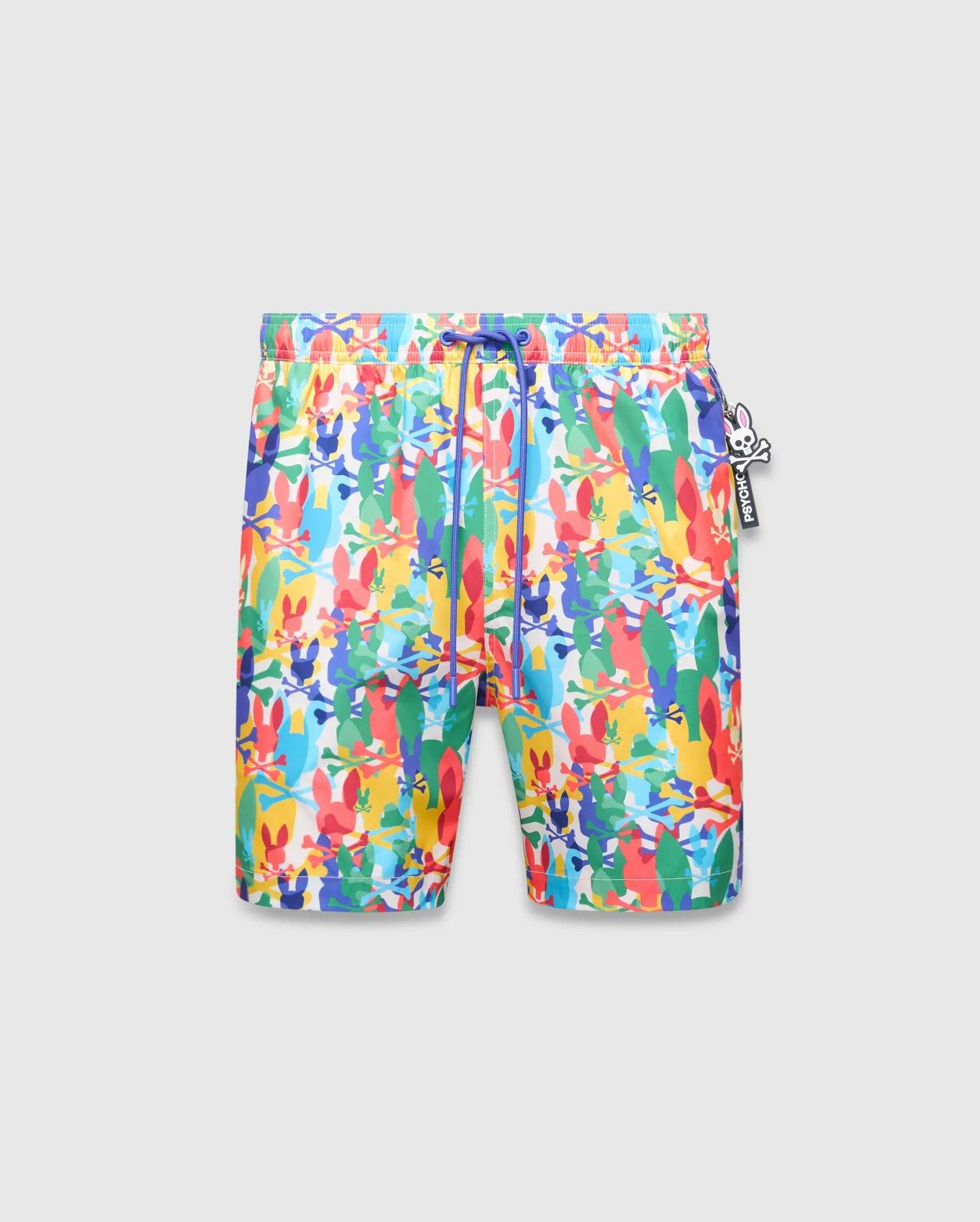 Mens Tanner Swim Trunk, a vibrant multi-color all-over print featuring Psycho Bunny skull logos and crossbones, with a blue drawstring and a distinct Psycho Bunny charm.