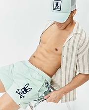 Mens Neo Swim Trunk 4 in pale mint green, featuring a large navy Psycho Bunny skull logo on the left leg, complemented by a cream textured striped shirt and a mint green Psycho Bunny trucker hat. (2)