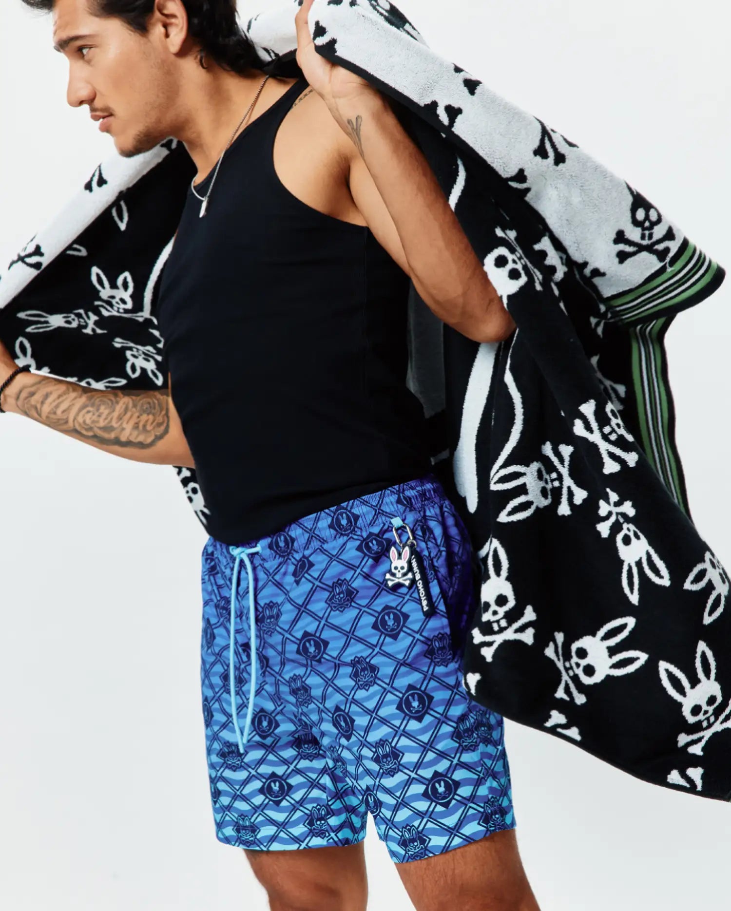 Mens Tobias Gradient Swim Trunk featuring an all-over blue geometric wave pattern with integrated small Psycho Bunny skull logos, light blue drawstring, and a Psycho Bunny keychain. (2)