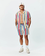Mens Hubert Swim Trunk in vibrant multi-color vertical stripes (pink, orange, yellow, blue, red), featuring a relaxed fit, textured quick-dry fabric, and a small embroidered Psycho Bunny skull logo on the left leg.