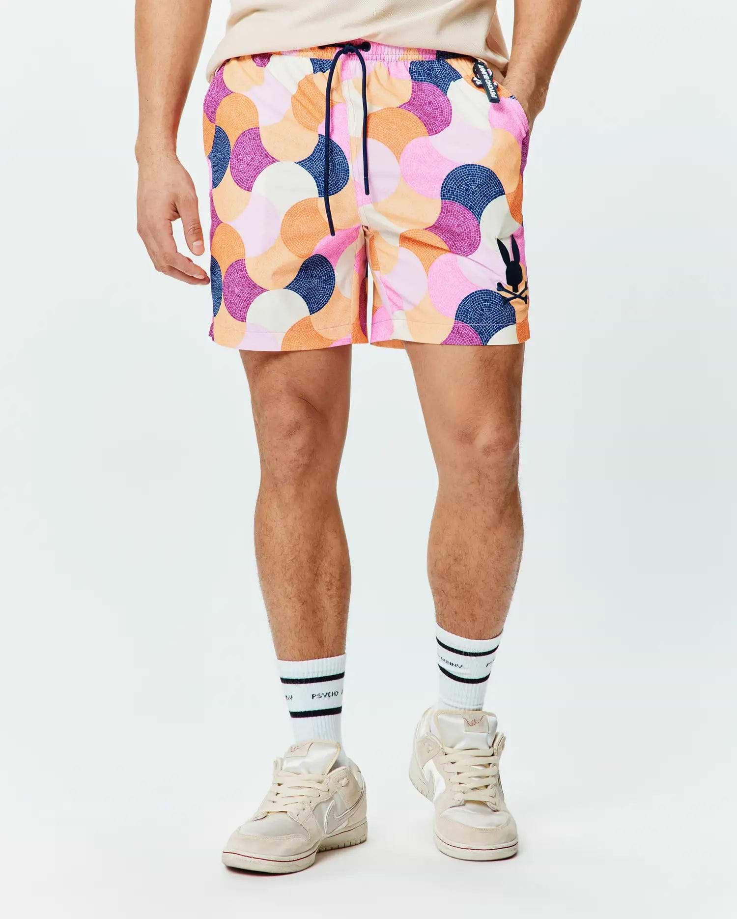 Mens Ethan Swim Trunk 6, featuring a vibrant multi-color abstract mosaic pattern in pink, orange, purple, and navy. Classic fit swim trunk with a black Psycho Bunny skull logo on the left leg and navy drawstring.