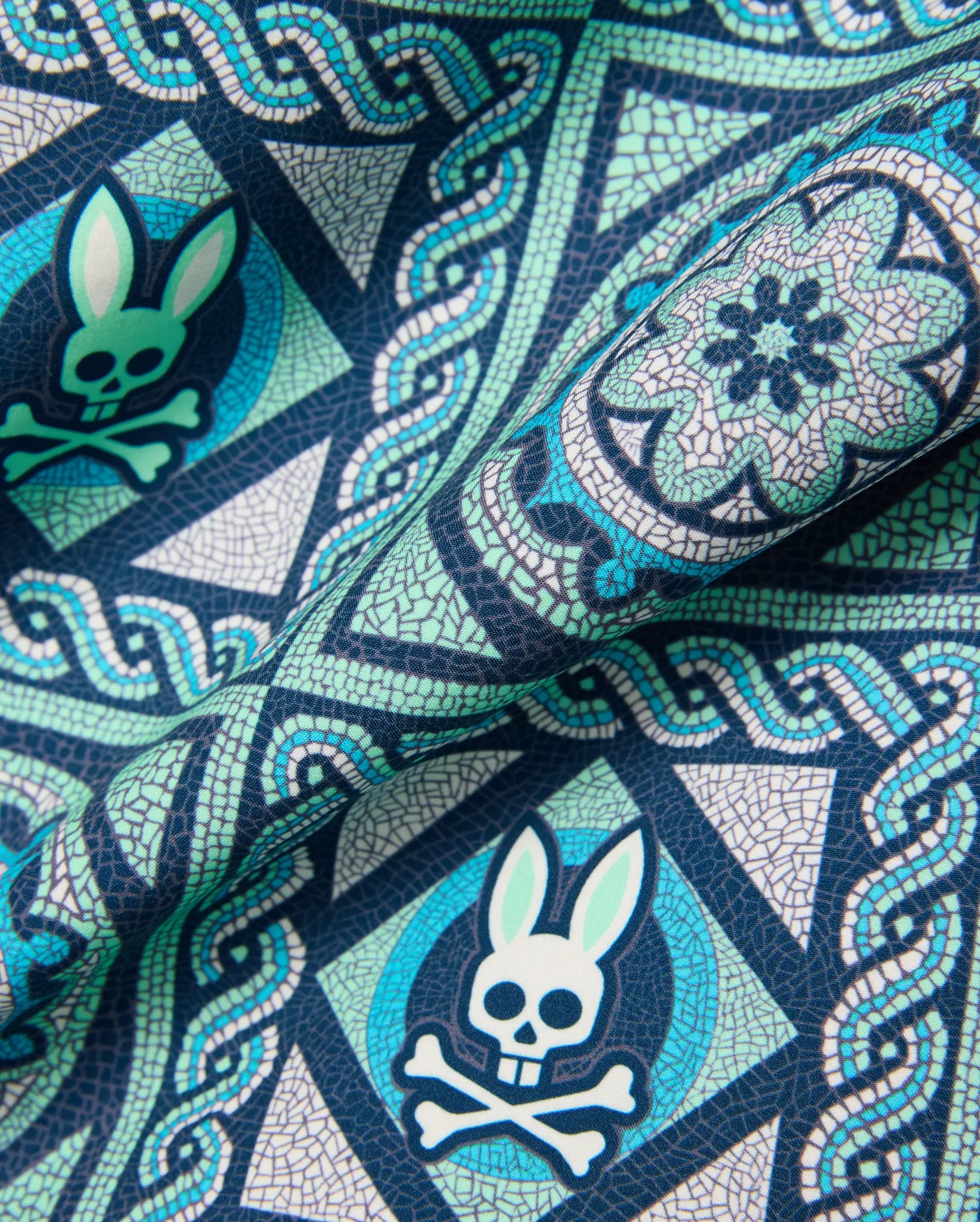 Mens Frank Swim Trunk 6, a navy blue fabric with a detailed mosaic print in teal, light green, and white, featuring the repeated iconic Psycho Bunny skull logo. (6)