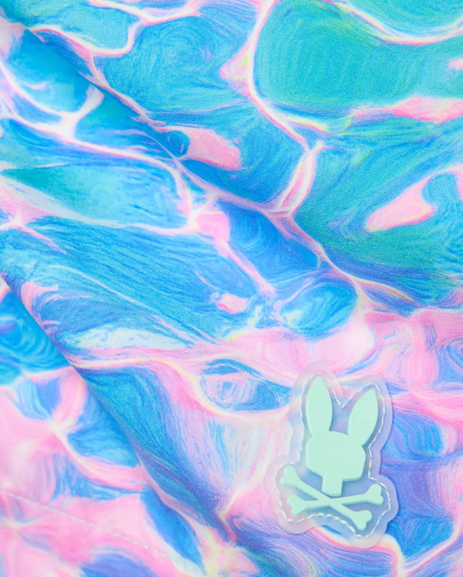 Mens Dayton Swim Trunk 6 featuring a vibrant blue and pink water ripple pattern on smooth fabric, accented by a small mint green rubberized Psycho Bunny skull logo patch. (6)