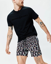 Black jersey t-shirt with large tonal PSYCHO BUNNY chest logo, paired with Mens Byron Swim Trunk 6 featuring an all-over print of colorful bunny skulls and crossbones on black, classic fit, with a small side tag. (3)