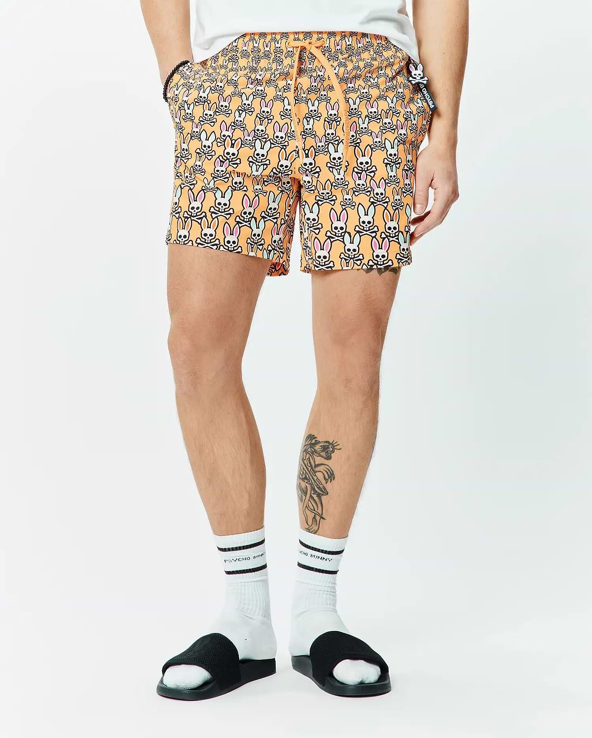 Mens Byron Swim Trunk 6, orange with all-over pink, light blue, white, and black Psycho Bunny skull pattern, classic fit, smooth fabric, small side logo tag.