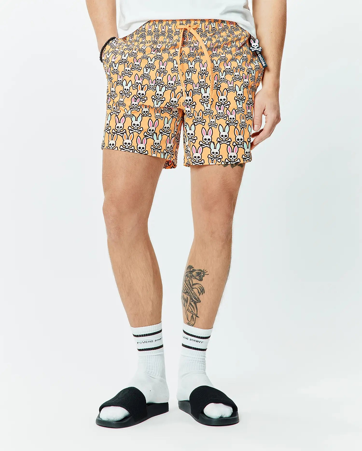 Mens Byron Swim Trunk 6, orange with all-over pink, light blue, white, and black Psycho Bunny skull pattern, classic fit, smooth fabric, small side logo tag.