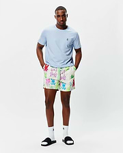 Light blue classic fit jersey t-shirt with small embroidered Psycho Bunny logo on left chest. Mens Quintin All Over Print Swim Trunk features an off-white base, vibrant multi-color graffiti-style bunny skull print, and neon green drawstring.