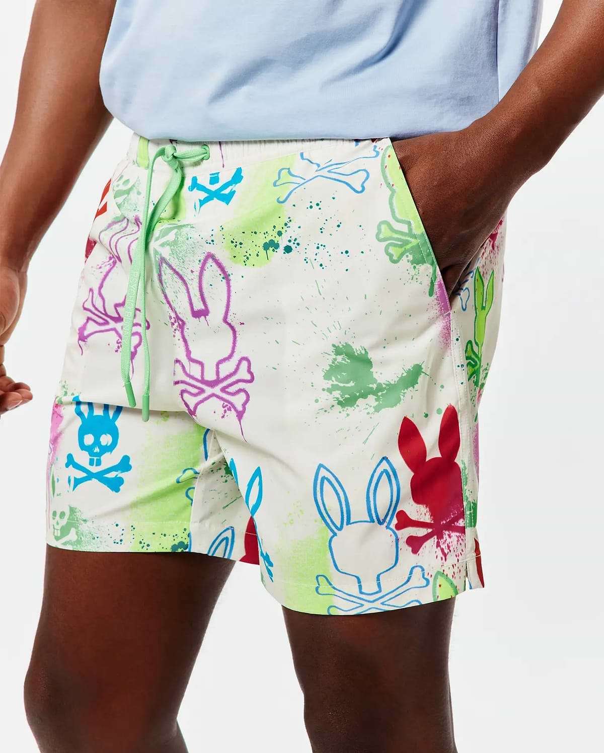Mens Quintin All Over Print Swim Trunk in white, with a vibrant multicolor paint splatter and outlined Psycho Bunny skull logo pattern, featuring a relaxed fit and green drawstring with PSYCHO BUNNY text.