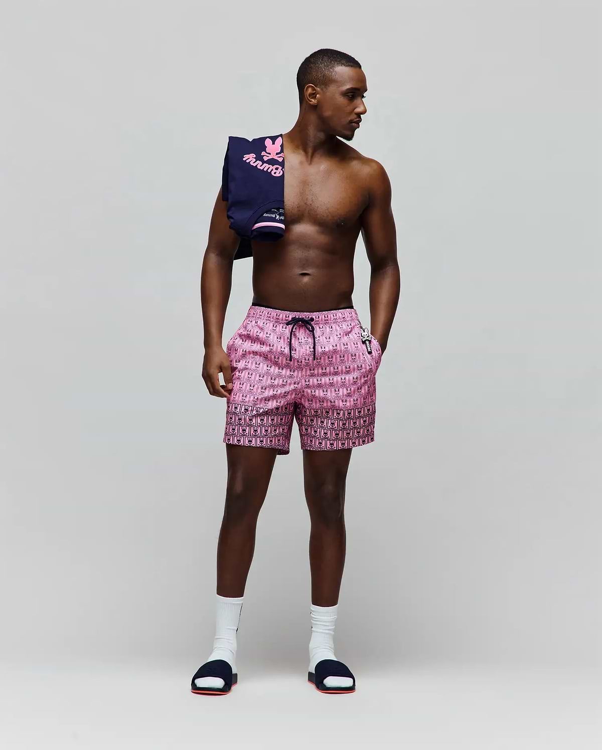 Mens Keon Swim Trunk in vibrant pink with an all-over black Psycho Bunny skull logo pattern, black drawstring, and a distinct black border at the hem. Classic fit, smooth fabric, small white logo. (4)
