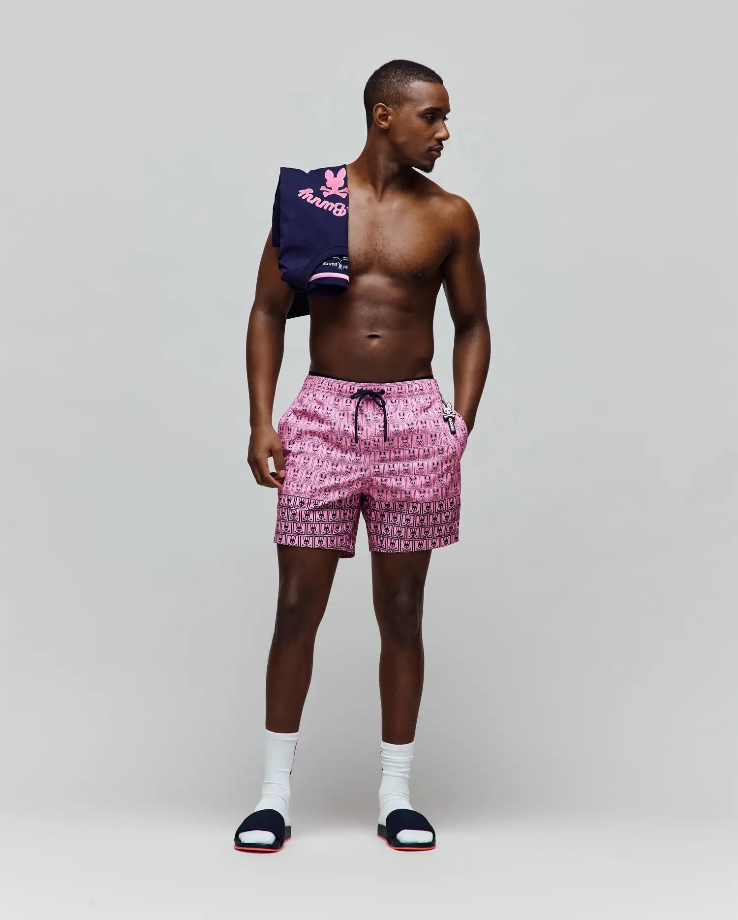 Mens Keon Swim Trunk in vibrant pink with an all-over black Psycho Bunny skull logo pattern, black drawstring, and a distinct black border at the hem. Classic fit, smooth fabric, small white logo. (4)