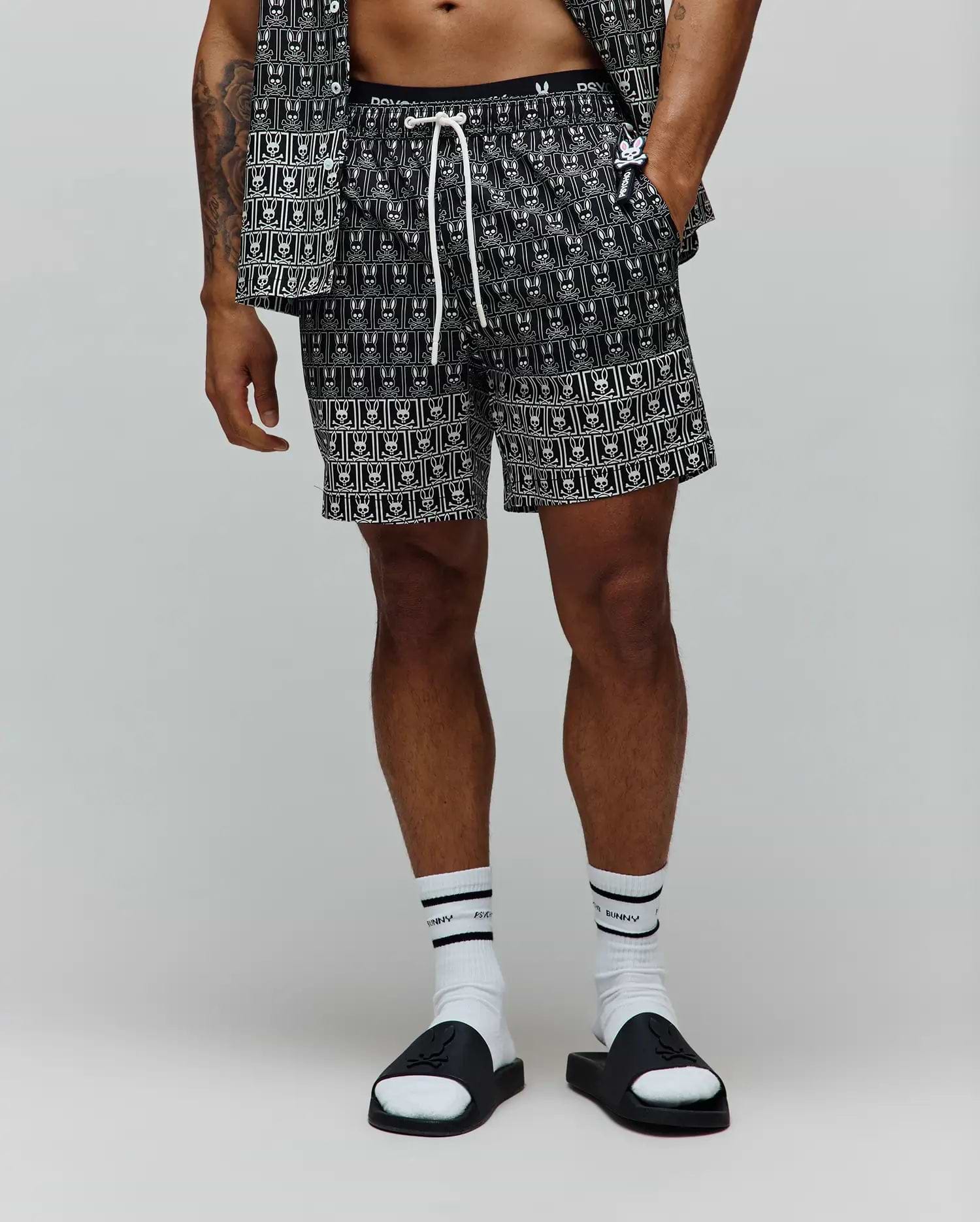 Mens Keon All Over Bunny Swim Trunk, black with a white all-over bunny skull pattern, classic fit, smooth woven fabric, featuring a white drawstring and a black elastic waistband with white Psycho Bunny text. (1)