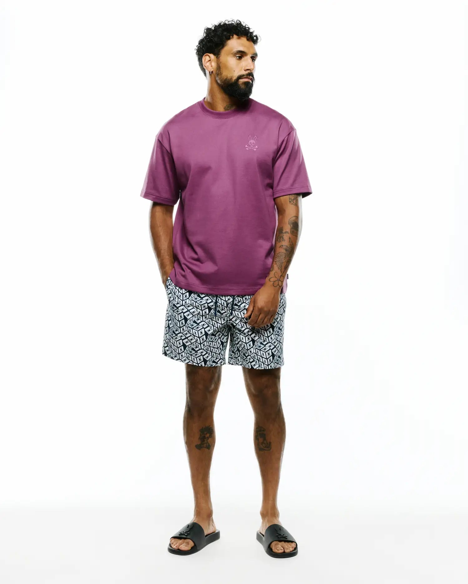 Relaxed fit plum jersey t-shirt with small tonal embroidered Psycho Bunny logo on left chest, paired with Mens Eddy All Over Print Swim Trunk featuring a black and white geometric pattern with integrated Psycho Bunny logos.